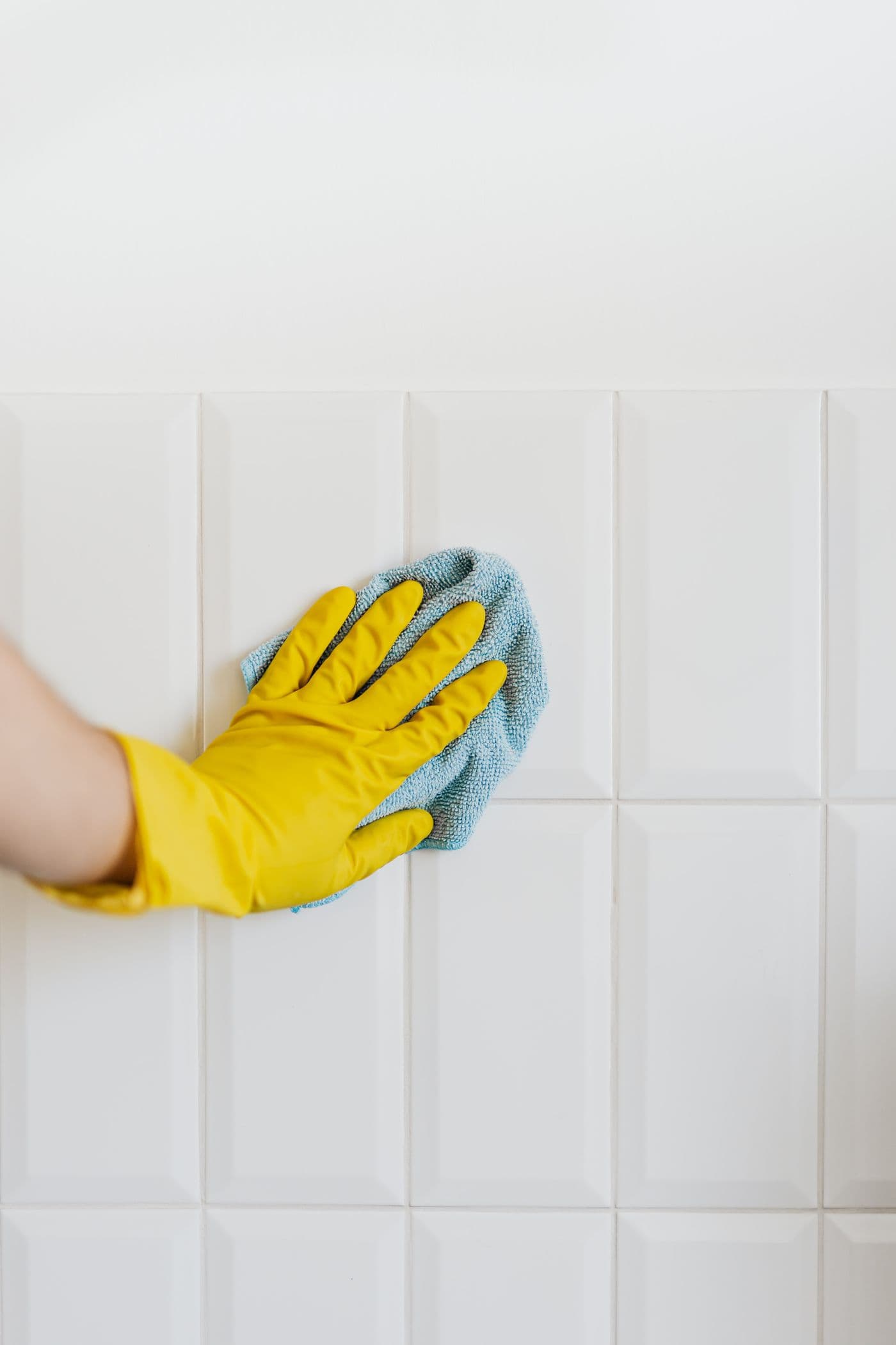 Main gantée nettoyant un mur carrelé blanc à la microfibre